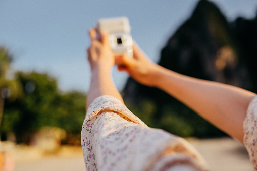 Side wide view Young influencer Asian Using smartphone and instant polaroid camera to sharing beautiful moment at seaside at sunset sea beach Phra nang beach in thailand