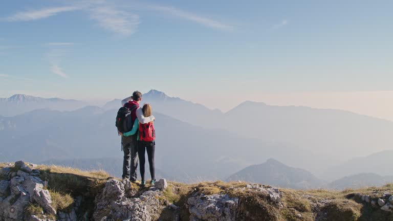 Hiker couple giving high five and hugging, looking at the mountains, aerial shot