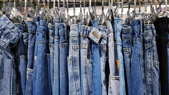 Many jeans or blue pants hanging on stainless steel hanger for sale at fashion shop. Collection of clothing and denim concept