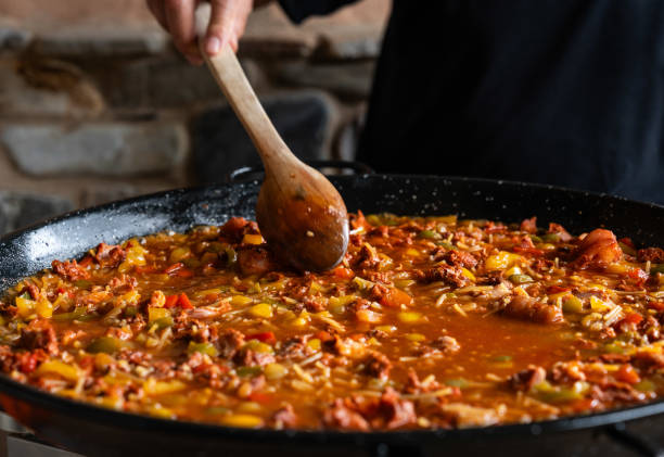 Fideua from Spain recipe, fry vegetables in a big paella pan with wood spoon Old man preparing Fideua from Spain recipe, fry vegetables in a big paella pan with wood spoon large pasta pot stock pictures, royalty-free photos & images
