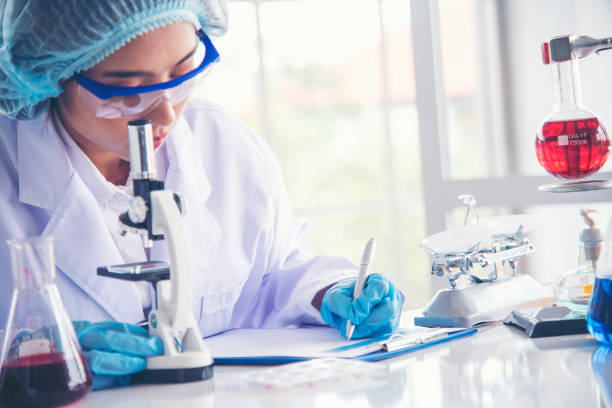 istock Asian Woman scientist hand write note research in medical lab look at science microscope medical test. Researcher biology chemistry. Asian Female technician laboratory using microscope blood test 1697138840