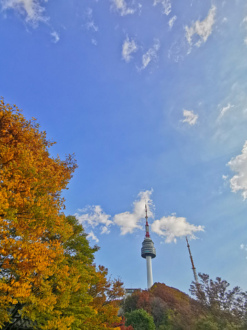 Seoul, South Korea - October 23, 2022: N Seoul Tourist Sigthseeing tall tower above Namsan mountain hill and blue sky with Autumn Foliage in orange green yellow leaves