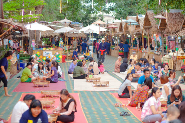 Classic thai food market stalls and eating thai people on traditional market Classic thai food market stalls and eating thai people on traditional market in Ratchaburi. Market is between trees near a temple. In center thai people are sitting on ground and are eating. Around are food market stalls. Market is seated next to temple  โบราณสถานวัดโขลง.  Market offers traditional thai food, thai clothes and other products and music and dance for public and visitors of market. true thailand classic stock pictures, royalty-free photos & images