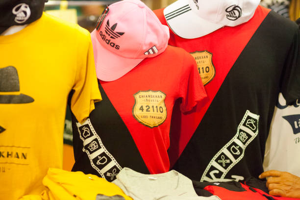 Shirts and caps at store in Chiang Khan in North Thailand. On shirts is emblem with Chiang Khan and postal zip code. On caps is Adidas logo. Fashion is placed on ventriloquist dummies outside of shop in in popular Walking Street