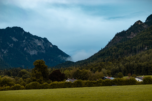 Misty clouds in between the mountains moving into the valley. Rainy weather at the German Alps region. Water vapor from the forest is in the air. Moody atmosphere in the nature.