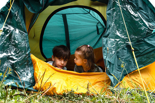 Portrait of boy and his sister while sitting in a tent in nature and looking away