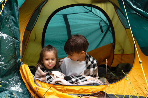 Portrait of cheerful children sitting in a tent and little girl shows her tongue to the camera