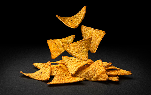 Falling spicy corn chips, hot Mexican nachos isolated on black background