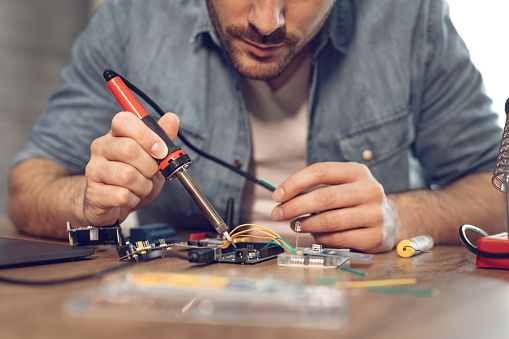 Engineer or technician focused on repair electronic circuit board with soldering iron.