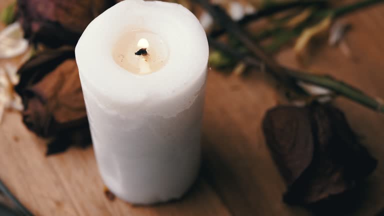 Burning White Candle and Four Withered Dry Roses Rotate on a Black Background