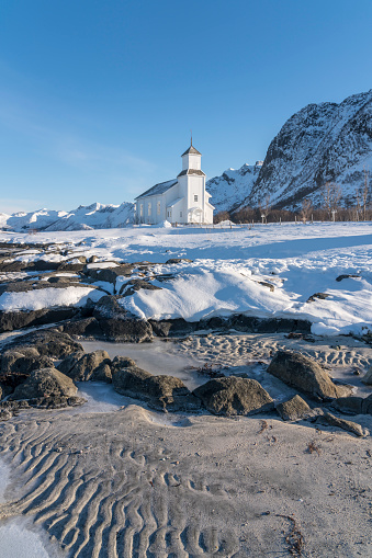 White wooden church at the coast in Gimsøy on Gimsoysand island in Lofoten archipelago in snow.