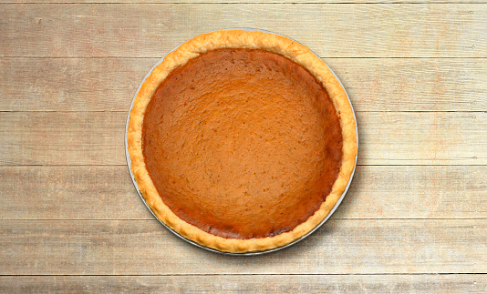 A Thanksgiving day pumpkin pie sitting on a rustic wood plank surface photographed from directly above.