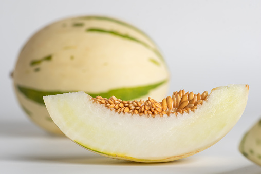 Ivory gaya melon with green dotted stripes and spots, and a slice of fruit on a white background. Close up