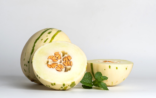 Ivory gaya melon with green dotted stripes and spots on a light background. Colorful ripe juicy and soft fruit, sweet taste with floral notes. Whole and half melons