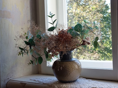 Composition of fresh and dried flowers in a vase on the windowsill.
