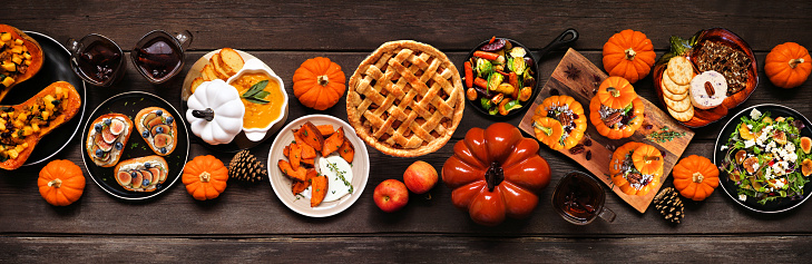 Delicious autumn meal table scene. Top down view on a dark wood banner background. Stuffed pumpkins and squash, sweet potatoes, appetizers, soup, vegetables and apple pie.