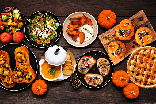 Delicious autumn meal table scene. Top view on a dark wood background. Stuffed pumpkins and squash, sweet potatoes, appetizers, soup, vegetables and apple pie.