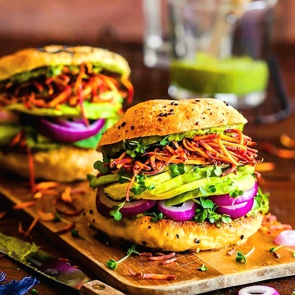 Keto diet veggie burger style sandwiches with avocado, red onions, sprouts, shredded carrots on poppy seed buns. Green juice in background.