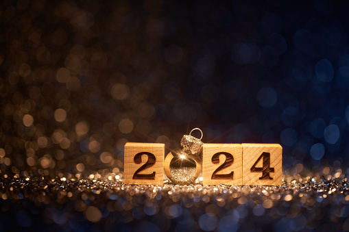 Low key photography of the number 2024 on wooden cubes surrounded by blue and gold sparkling defocused lights. Native image size: 7952x5304