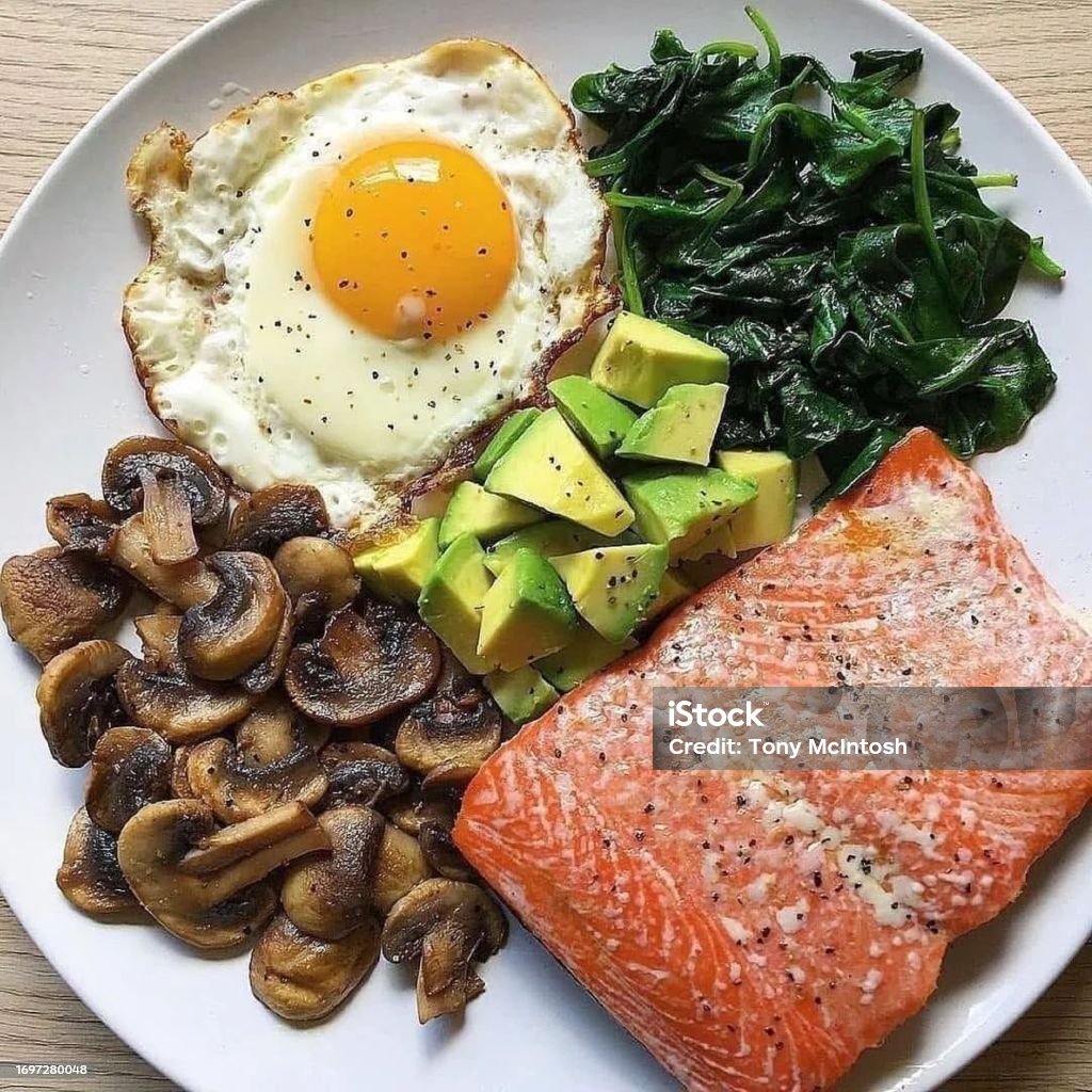 Anytime Meal Salmon, fried egg, avocado chunks and sautéed mushrooms and spinach on plate on table. Ketogenic Diet Stock Photo