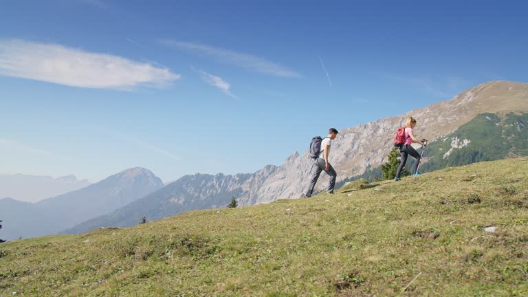 Couple trekking, walking uphill with a view of a mountain range, handheld shot