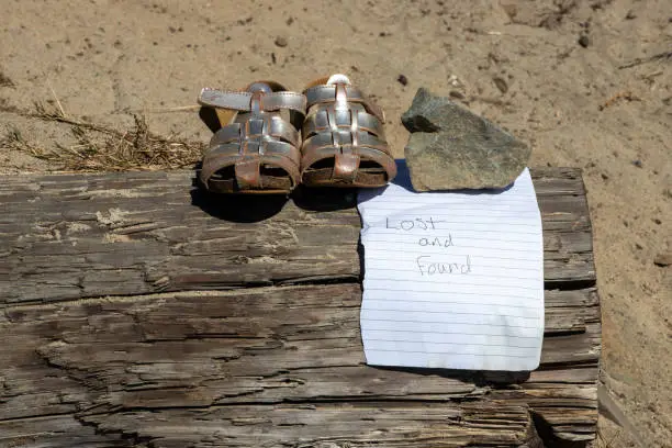 Lost and Found sand covered sandals along the beach with a note