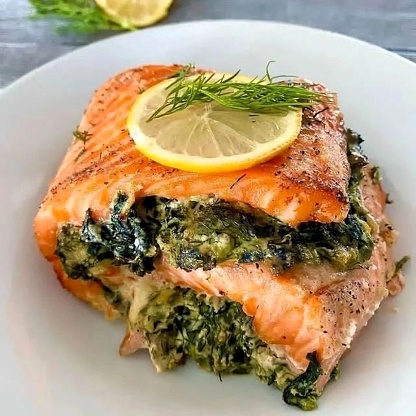 Grilled salmon filet stuffed with creamed spinach, lime slice and garnish on plate.
