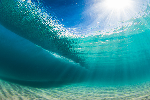 Underwater view beneath a wave breaking on sand in crystal clear water. Photographed in South Western Australia.