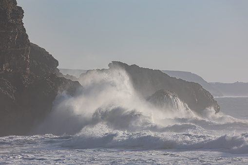 Big ocean waves crash against rocks. Mid shot
