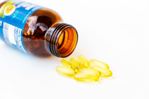 Pile of yellow fish oil capsules and pill glass bottle, fish oil contains omega-3 fatty acids, EPA and DHA, which reduce inflammation in the body, isolated on white background