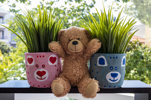 Small teddy bear sitting between two painted flower pots