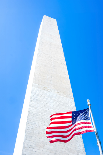 Washington Monument in Washington DC, United States with American flag waving in front.