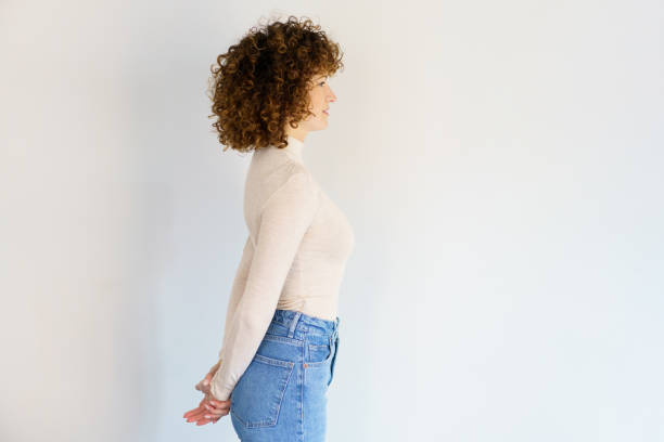 Curly haired woman standing with hands behind back stock photo