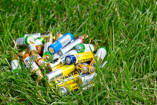 Nizhniy Novgorod, Russia, July 2023. Used alkaline batteries on green grass. Environmental pollution problem concept. Toxic waste and recycling.