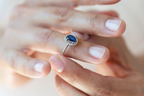 Hand of an unrecognizable female is about to wear a sapphire ring.