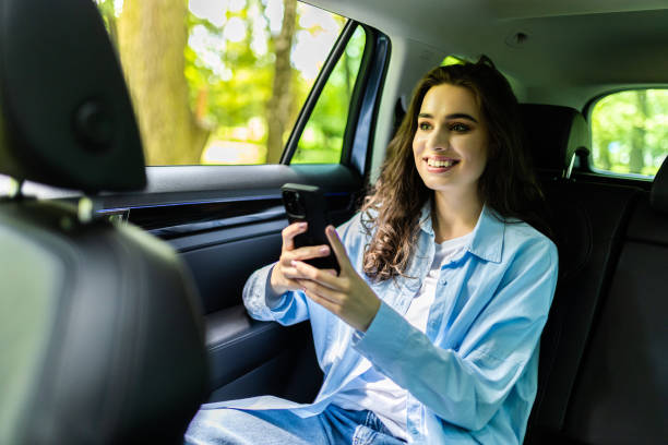 istock Beautiful woman is using a smart phone and smiling while sitting on back seat in the car 1697518489