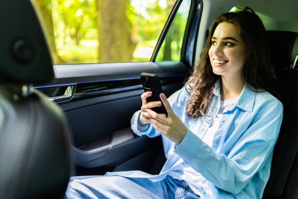 istock Beautiful woman is using a smart phone and smiling while sitting on back seat in the car 1697526653