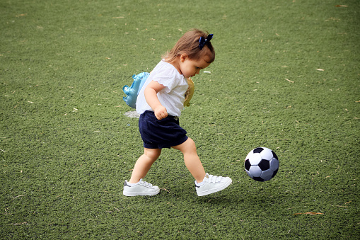 Beautiful three year old girl playing football and kicking the ball to the bow.