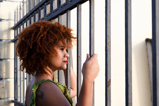 Portrait of the face of a beautiful woman with red hair looking at the sun through an iron railing. Happy person traveling.