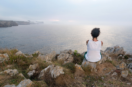 Asturias, Spain. 08/23/2023. Woman contemplating the sunset from the cliffs. Asturias