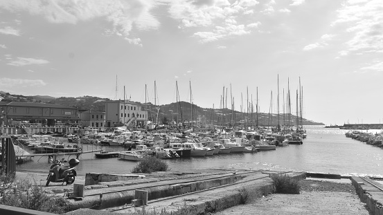 wide black and white view of the port of Sanremo in summer. A Vespa is parked and behind there are the boats