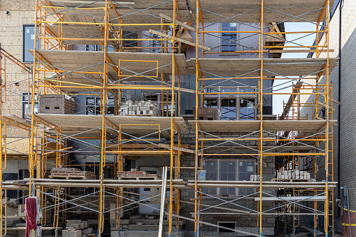 Close-up of yellow scaffolding and building materials at construction site - windows of partially constructed building in background - daytime. Taken in Toronto, Canada.