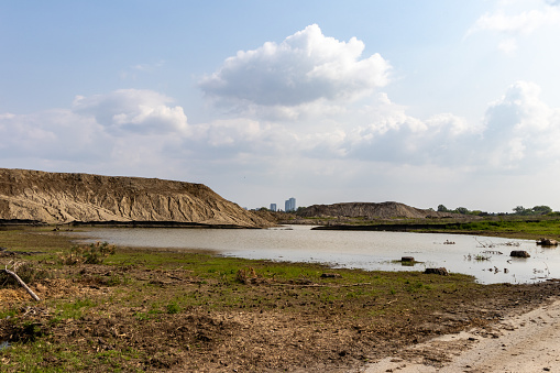 Barren landscape with water and city skyline - dry, cracked earth and hill with rocks - blue sky with clouds. Taken in Toronto, Canada.