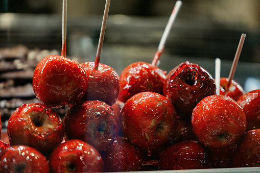 Shiny red caramel apples, stacked enticingly in a display window, glisten with oozing sugar. A caloric and indulgent treat, they are a quintessential snack for tourists looking for a walking delight