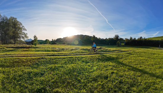 Wide angle shot of a woman cycling in the backlight of the sun. Sport in evening light