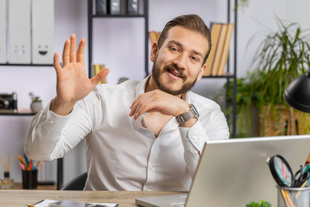 istock Businessman working on laptop smiling friendly at camera and waving hands gesturing hello at office 1697804596