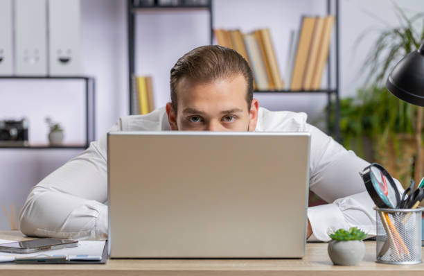 istock Lebanese confident businessman hiding behind laptop computer, looking at camera, spying, peeping 1697804604