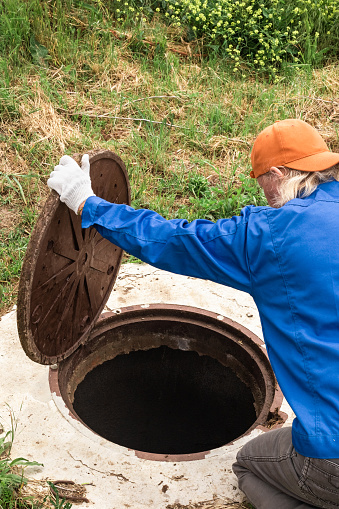 a worker checks a plumbing well in the countryside. Maintenance and cleaning of septic wells.