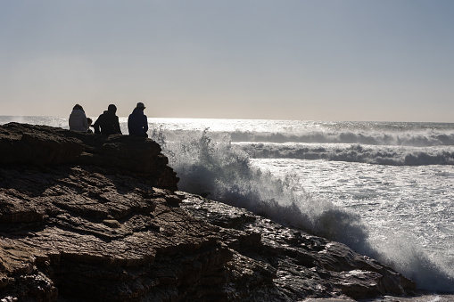 28 February 2023 Nazare, Portugal: People sit on rocks and look at the sea. Mid shot