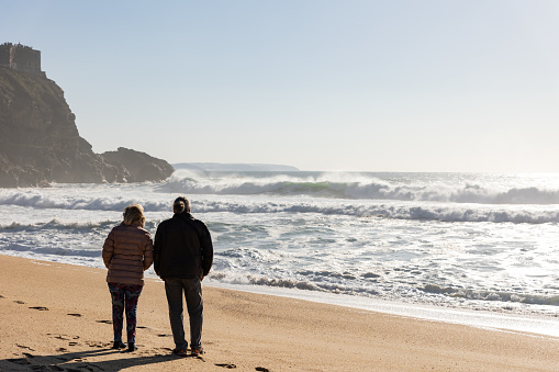 28 February 2023 Nazare, Portugal: An adult couple walking on the beach during a storm. Mid shot